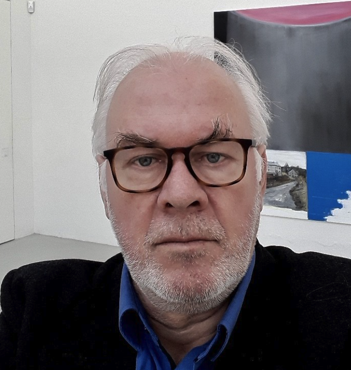 Close-up portrait of an older man with glasses and gray hair, displaying a serious expression, set against a modern art background.