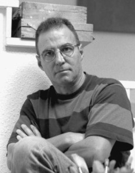 Black and white portrait of a man wearing glasses and a striped shirt, sitting with his arms crossed.