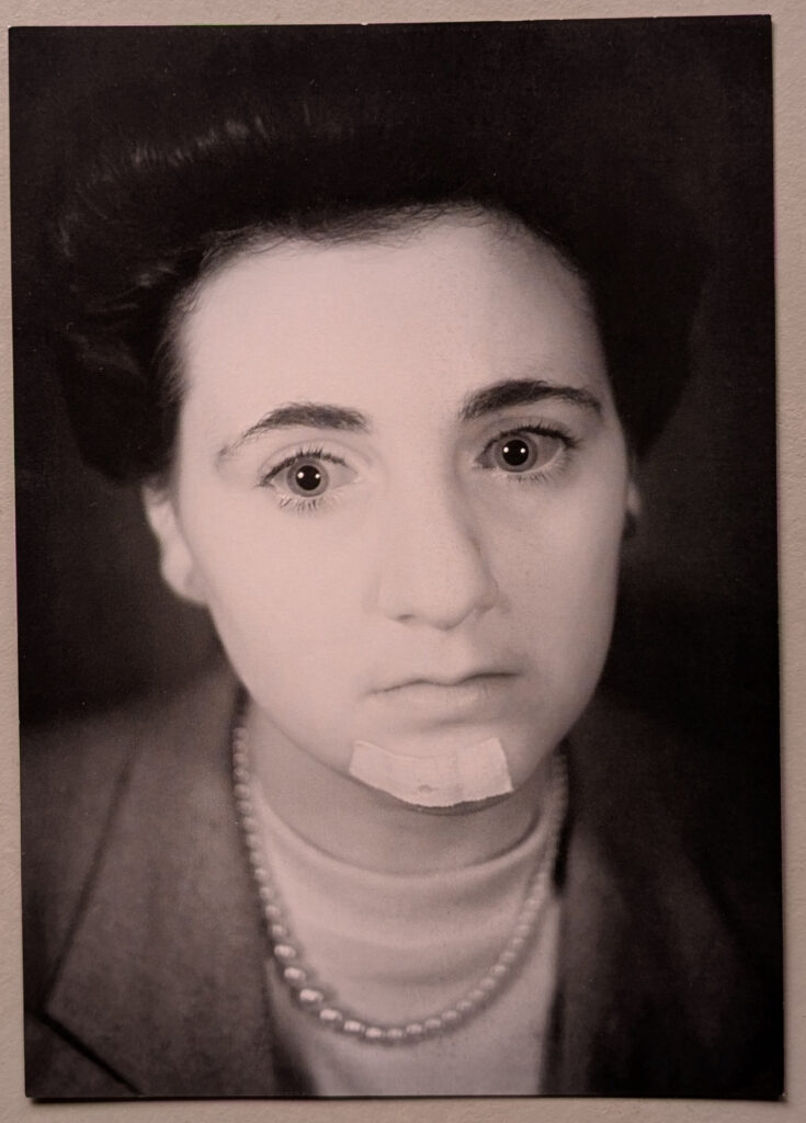 A black and white portrait of a young woman with a serious expression, wearing a pearl necklace and a sweater. She has a slight bandage on her chin and is dressed in a formal jacket.