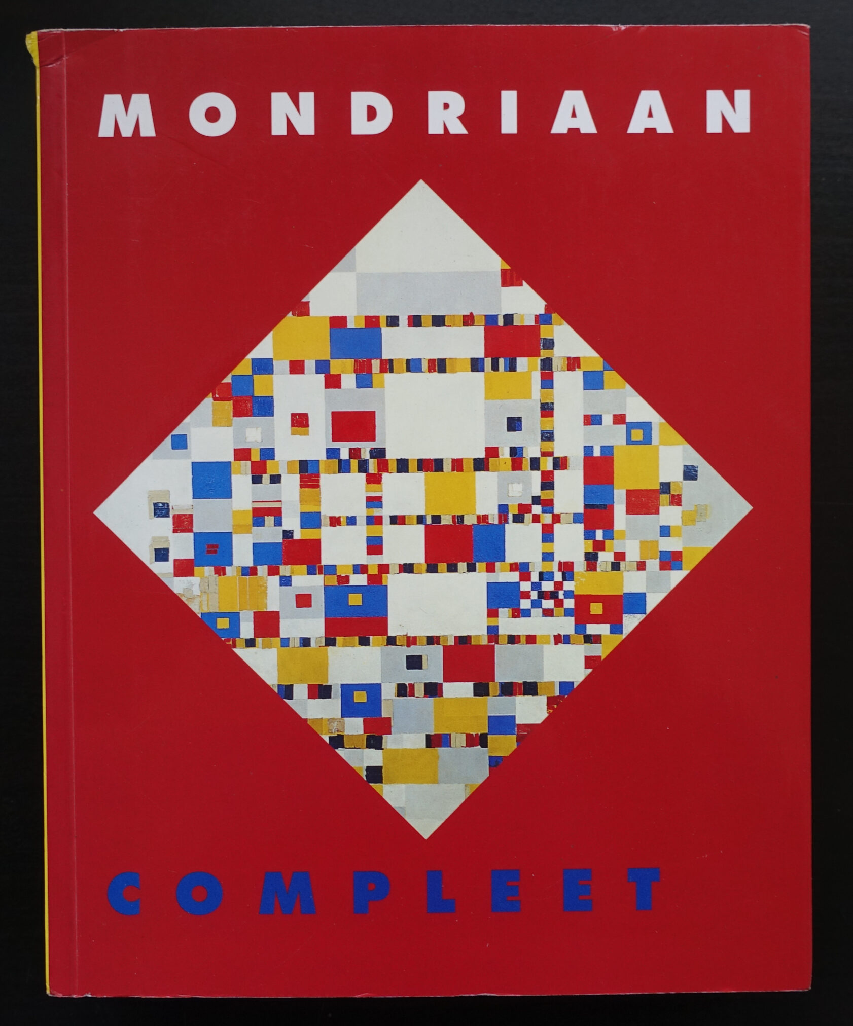 Cover of the book titled 'Mondriaan Compleet' featuring a colorful geometric pattern on a red background.