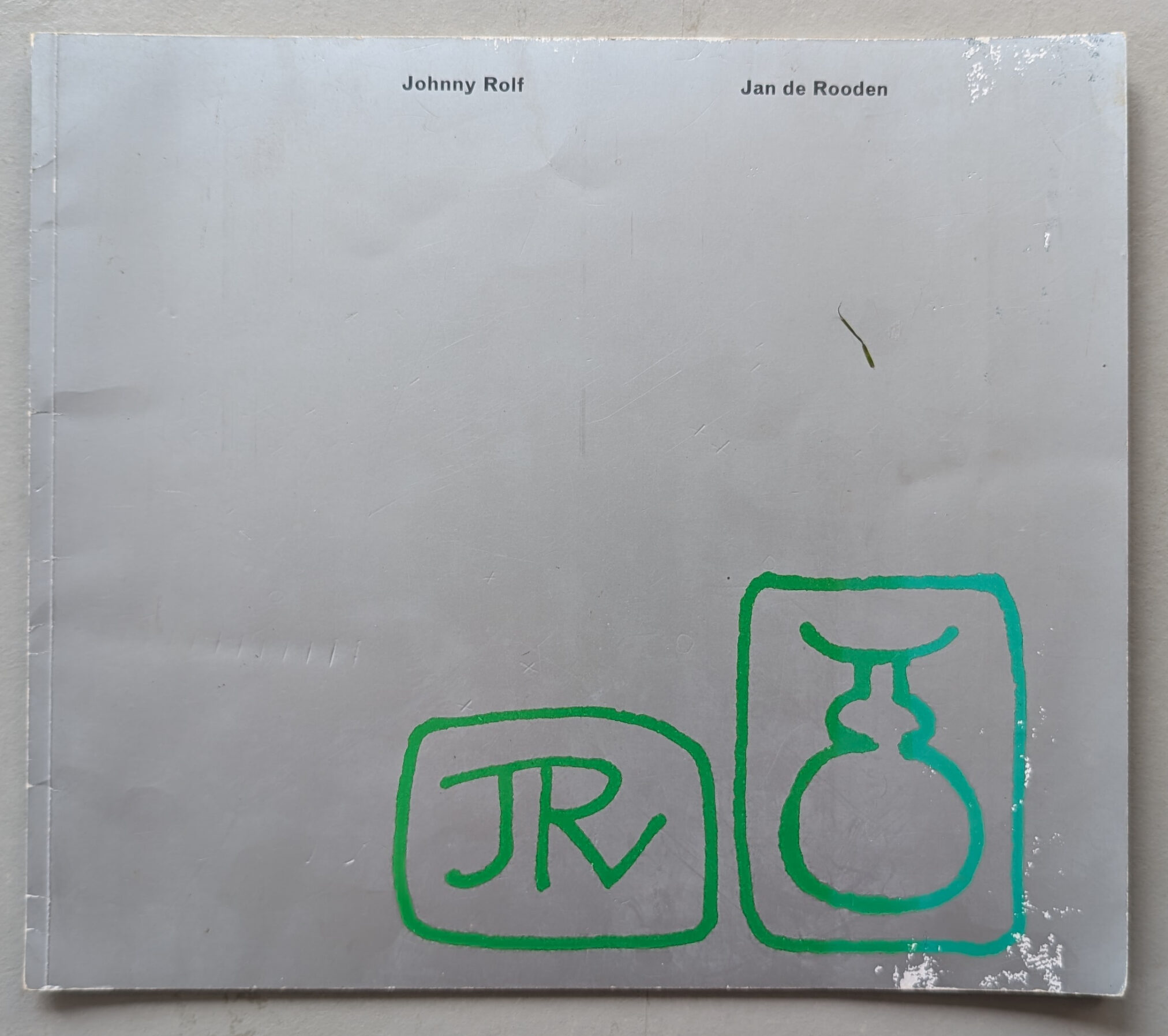 Cover of a book featuring the names 'Johnny Rolf' and 'Jan de Rooden' with a simple green graphic design including the initials 'JR' and a vase illustration.