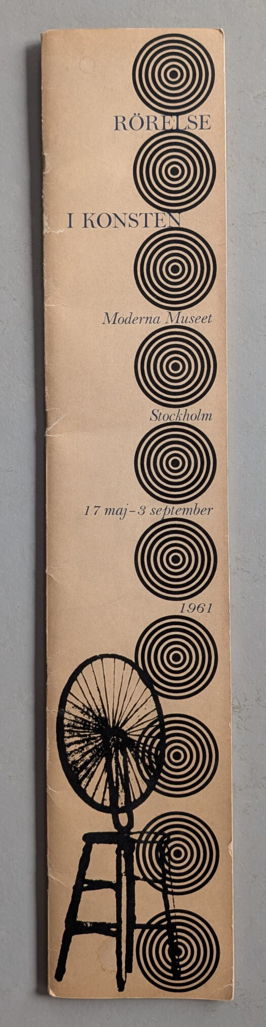 A vintage exhibition brochure titled 'Rörelse i konsten' featuring concentric circles and an image of a bicycle wheel on a wooden stool.