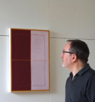A man observing a rectangular abstract painting featuring maroon and light pink sections mounted on a wall.