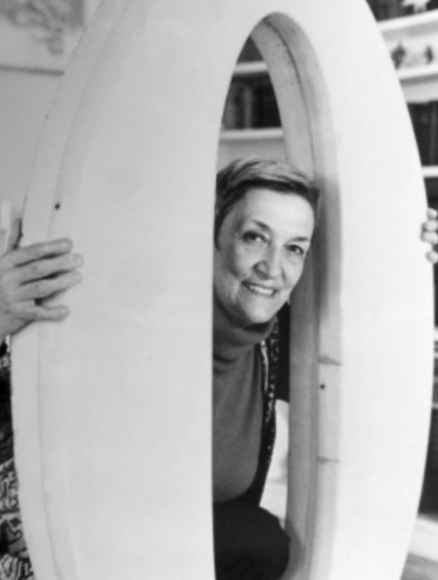A woman smiling while peeking through a large, oval-shaped frame.