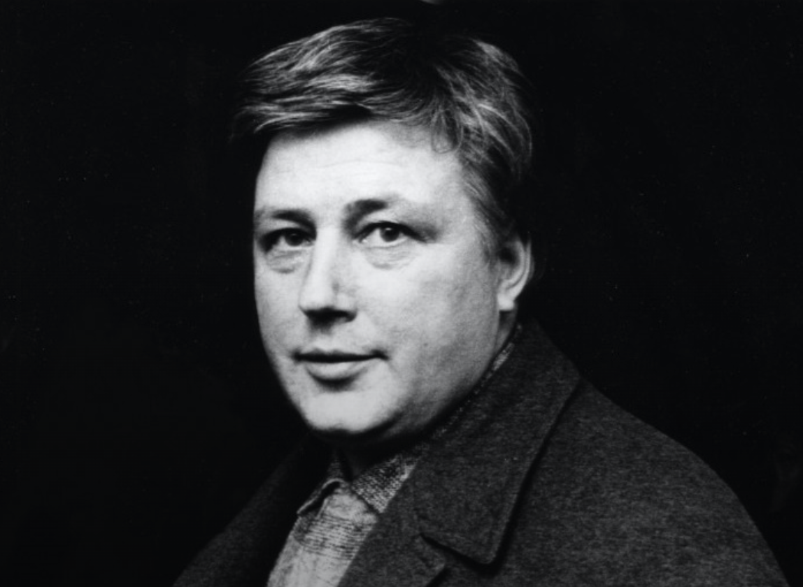 A close-up black and white portrait of a man with short hair, wearing a collared shirt and a coat, looking directly at the camera.