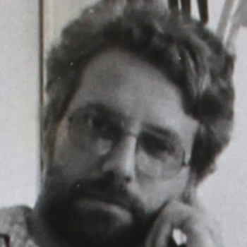 A close-up black and white portrait of a man with glasses and a beard, thoughtfully resting his chin on his hand.