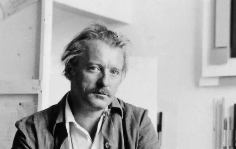 Black and white portrait of a man with light hair and a mustache, seated indoors with a thoughtful expression.