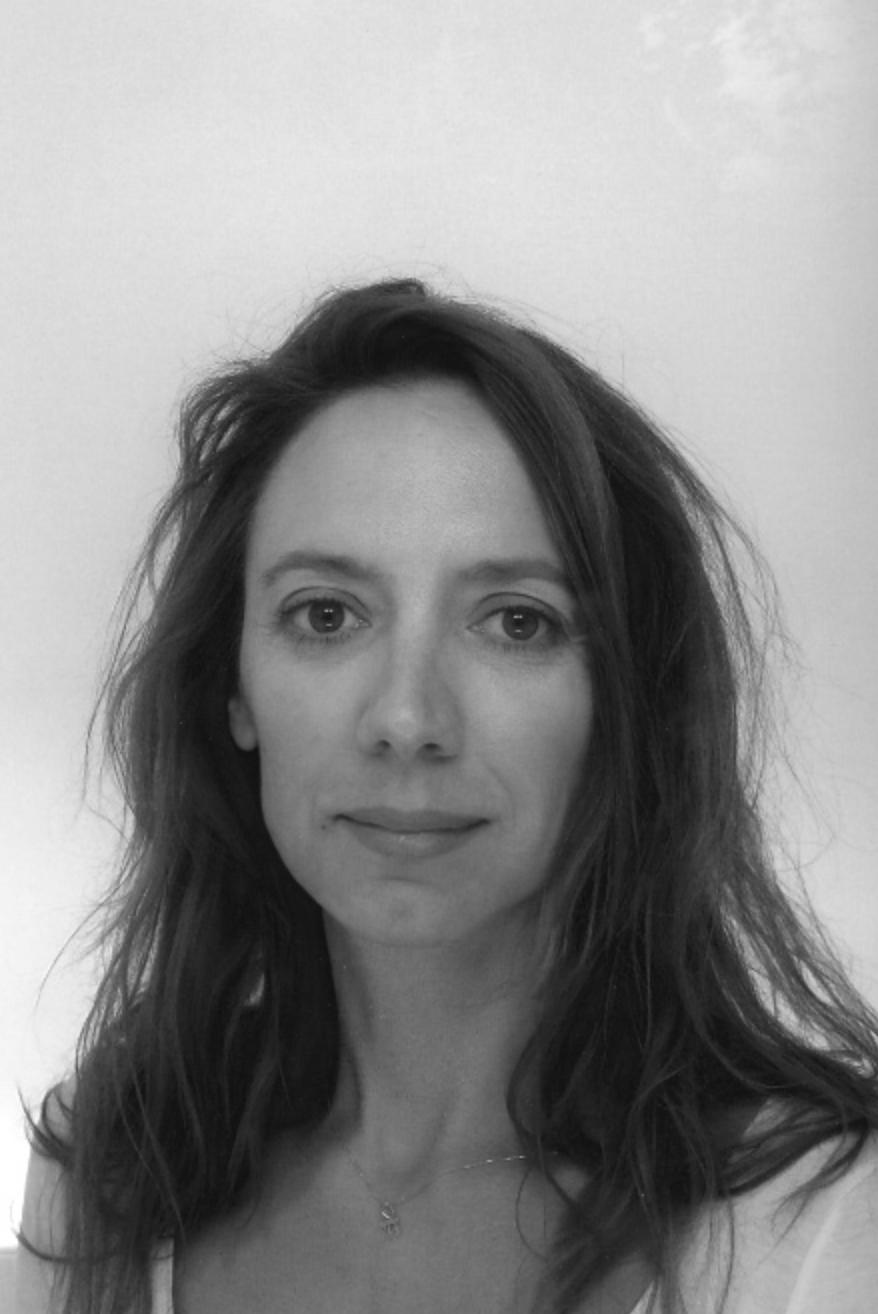 A portrait of a woman with long, dark hair, looking directly at the camera against a light background.