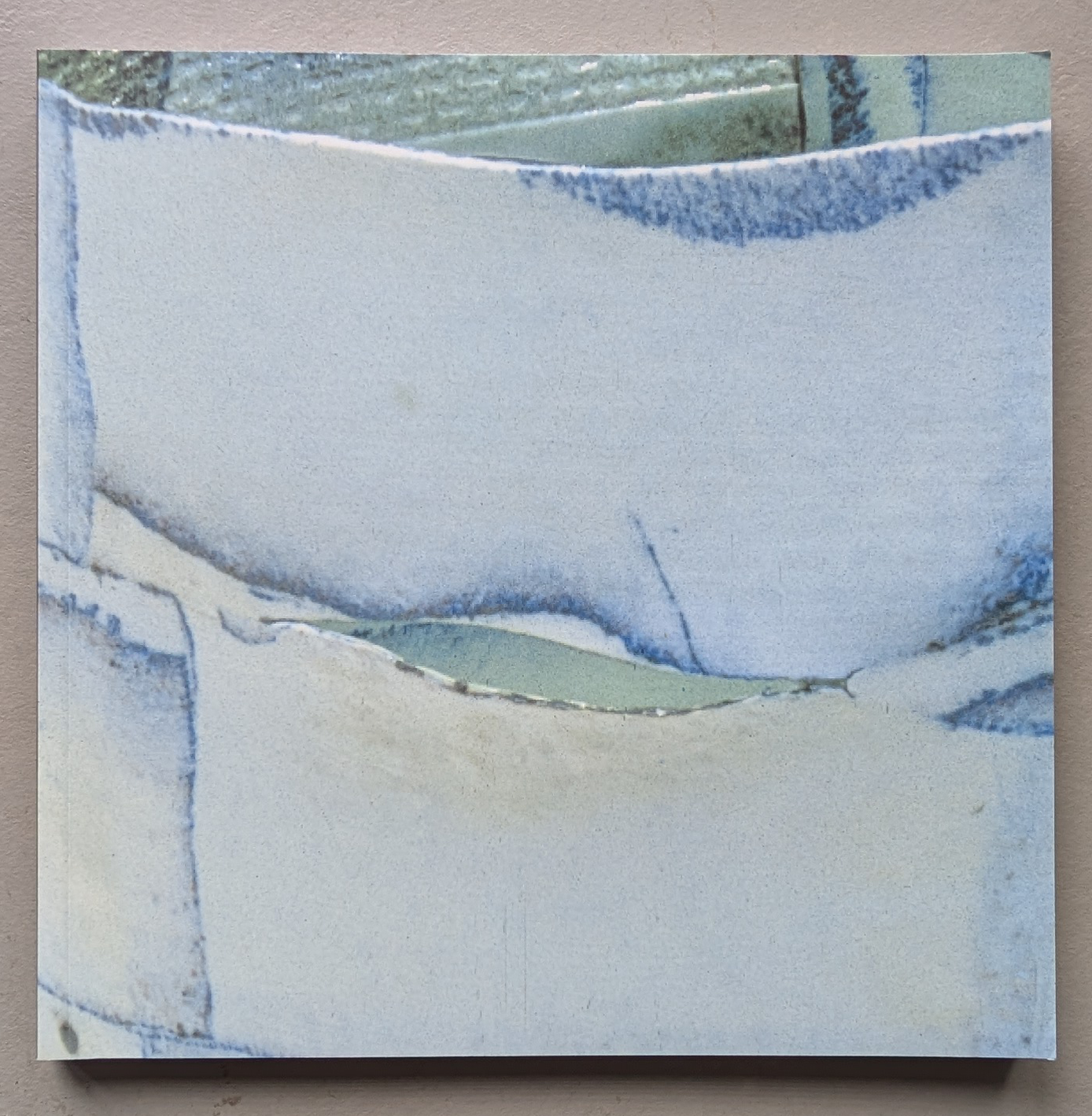 Close-up image of a delicate porcelain artwork featuring thin, white surfaces with vibrant blue and green accents, displaying intricate lines and textures.