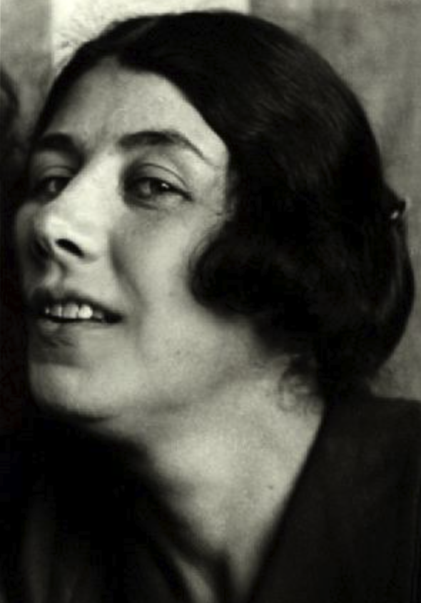 Portrait of a woman with dark, wavy hair and a slight smile, looking over her shoulder.