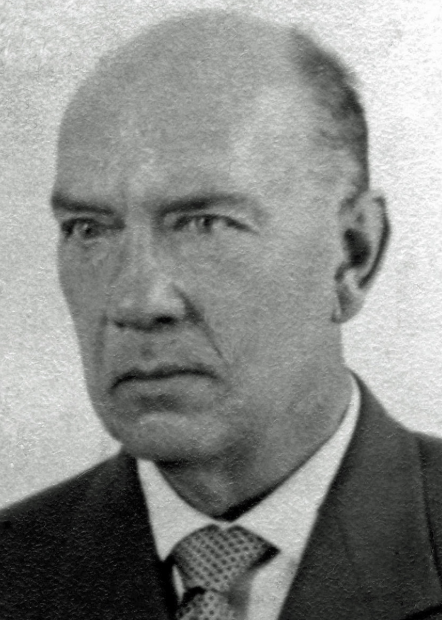 A black and white portrait of a serious-looking middle-aged man in a suit and tie, with thinning hair and a stern expression.