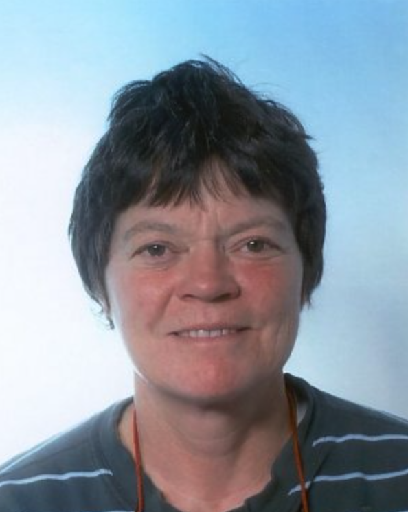 A woman with short, dark hair and a friendly smile, wearing a striped shirt against a light blue background.