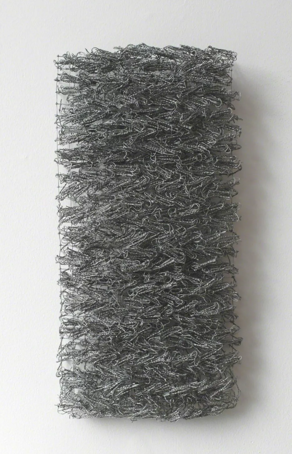 A textured artwork composed of intertwining gray wire, mounted on a white wall.