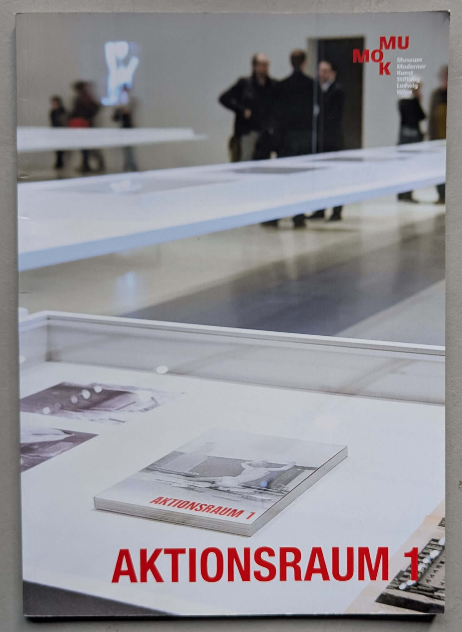 Cover of the Aktionsraum 1 exhibition catalog featuring displayed photographs and a book titled 'Aktionsraum 1'.