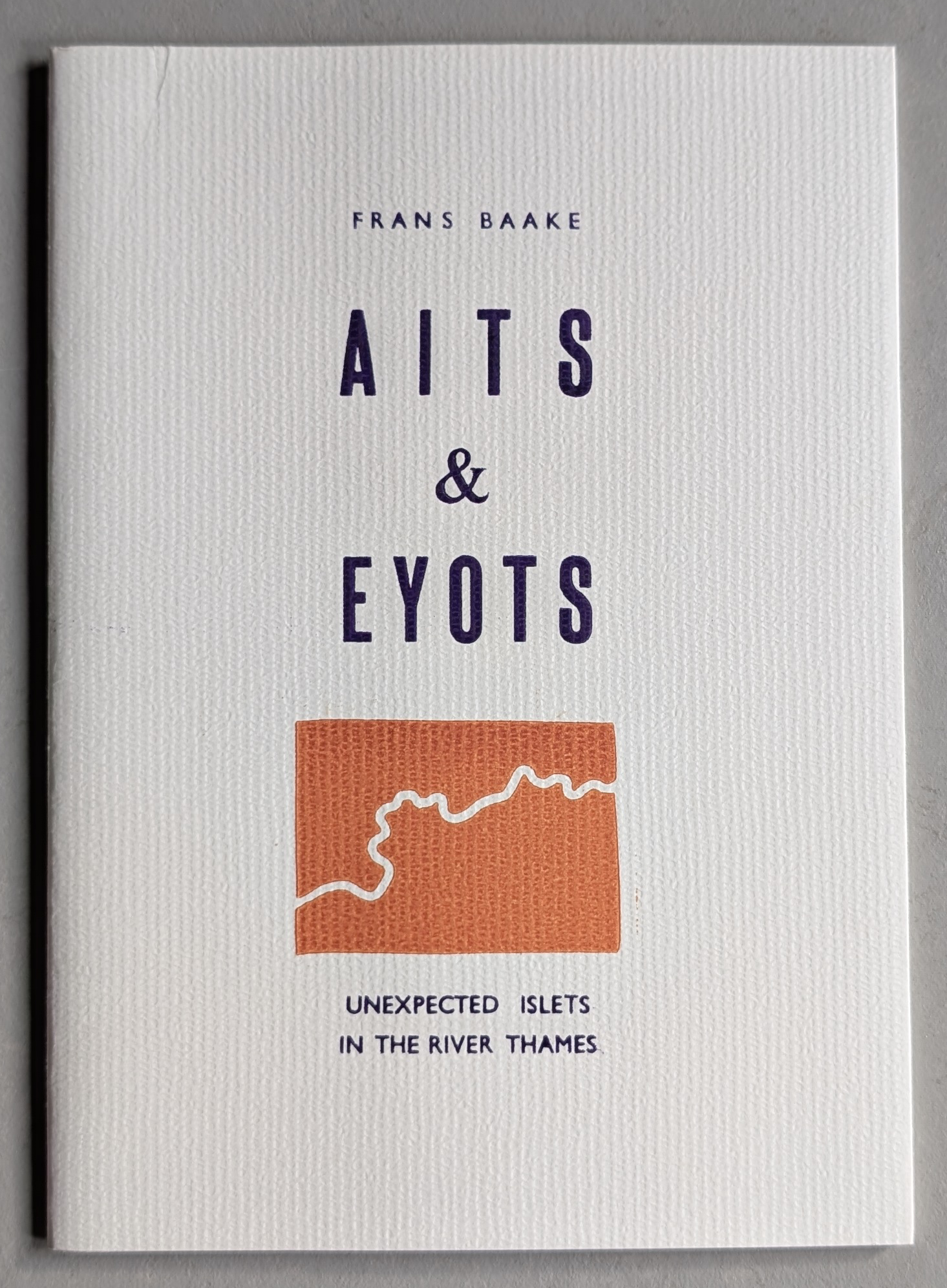 Cover of the artist book 'Aits & Eyots' by Frans Baake, featuring a textured white background, a stylized illustration of an islet, and the subtitle 'Unexpected Islets in the River Thames.'