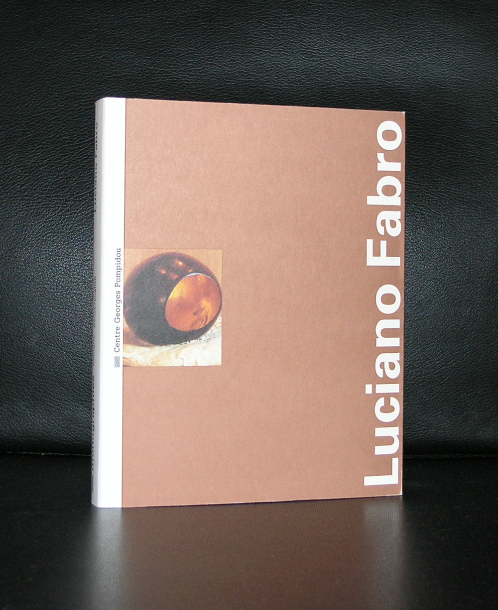 A book titled 'Luciano Fabro' with an artistic cover depicting a circular object on a textured surface, resting against a dark background.