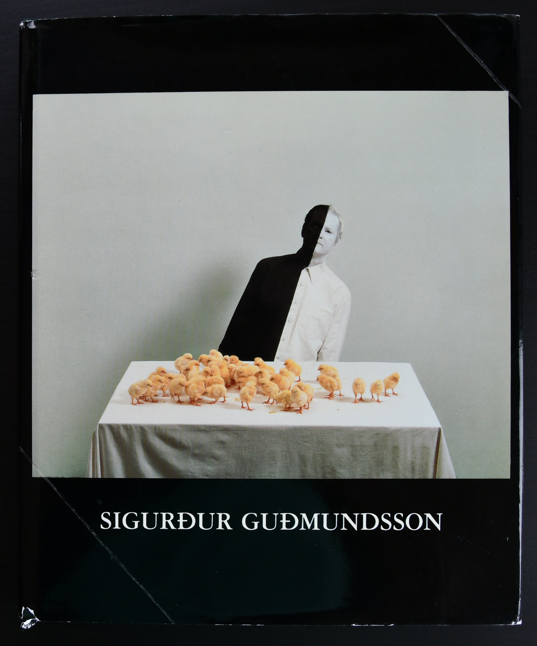 Book cover featuring a half-visible figure against a white backdrop, surrounded by numerous small chick figurines on a table with a white cloth.