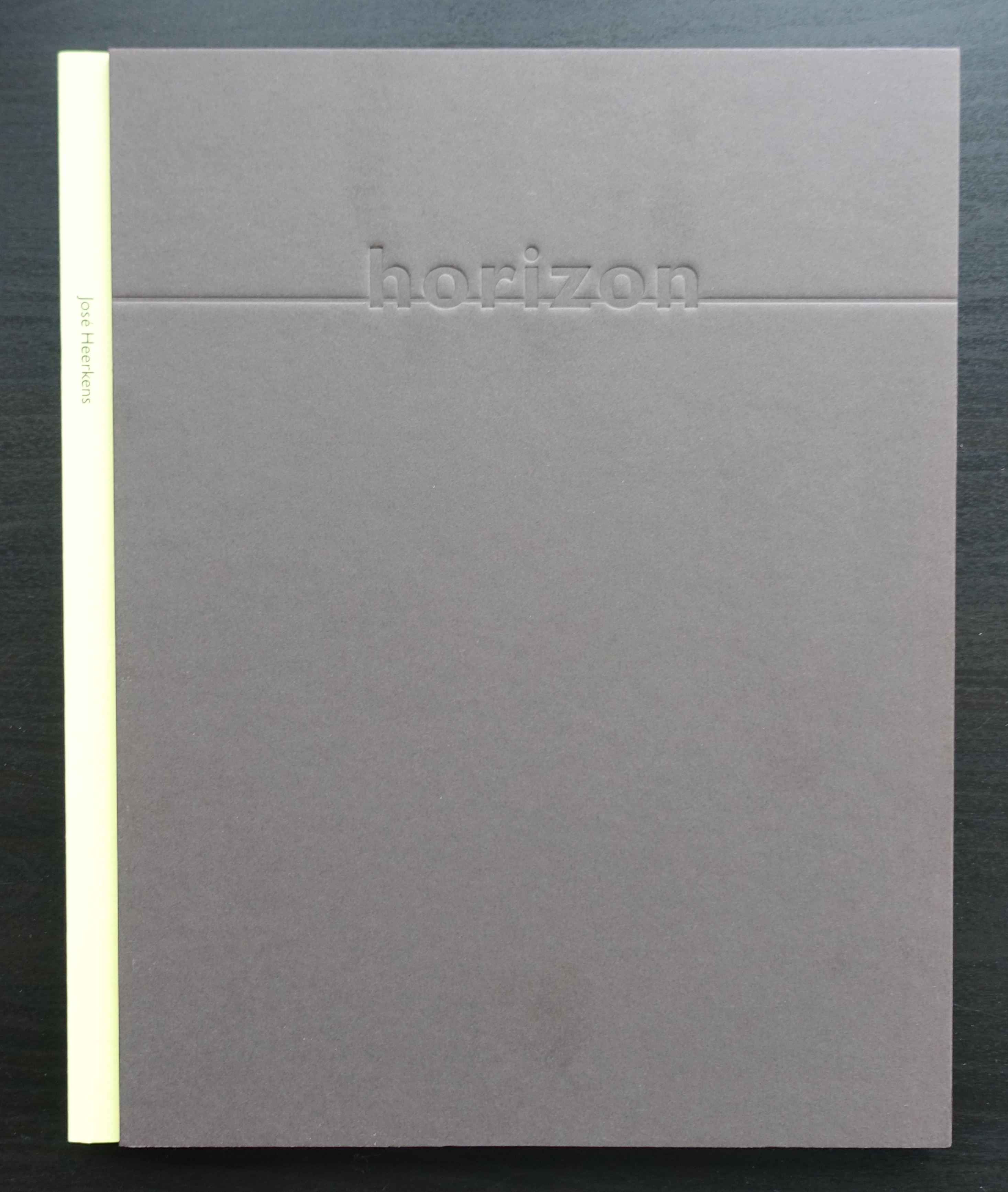 A closed book titled 'horizon' by José Heerkens, featuring a gray cover with embossed lettering and a yellow spine.