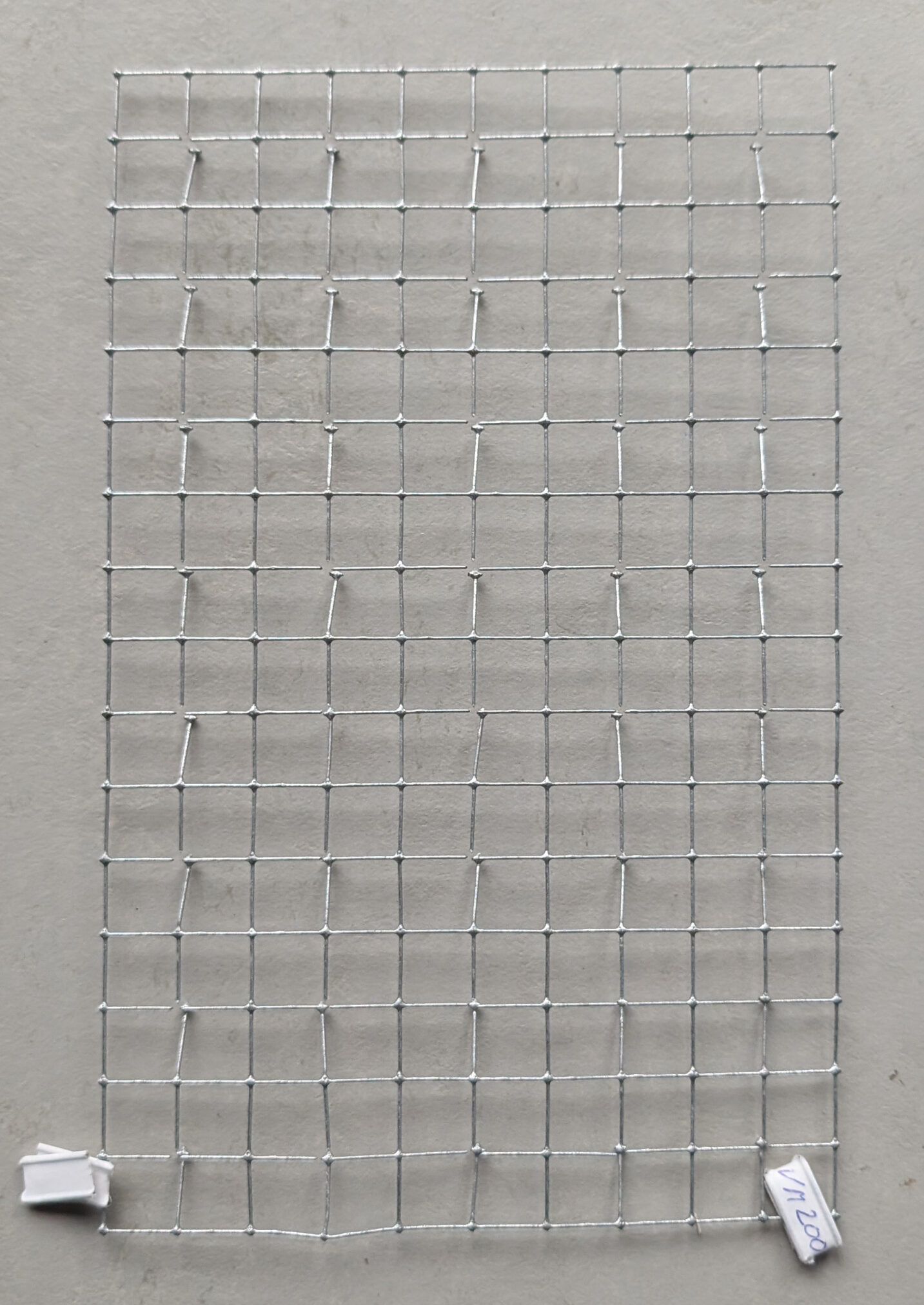Close-up of a galvanized square mesh with a 12 x 12 mm grid pattern, shown against a light background.