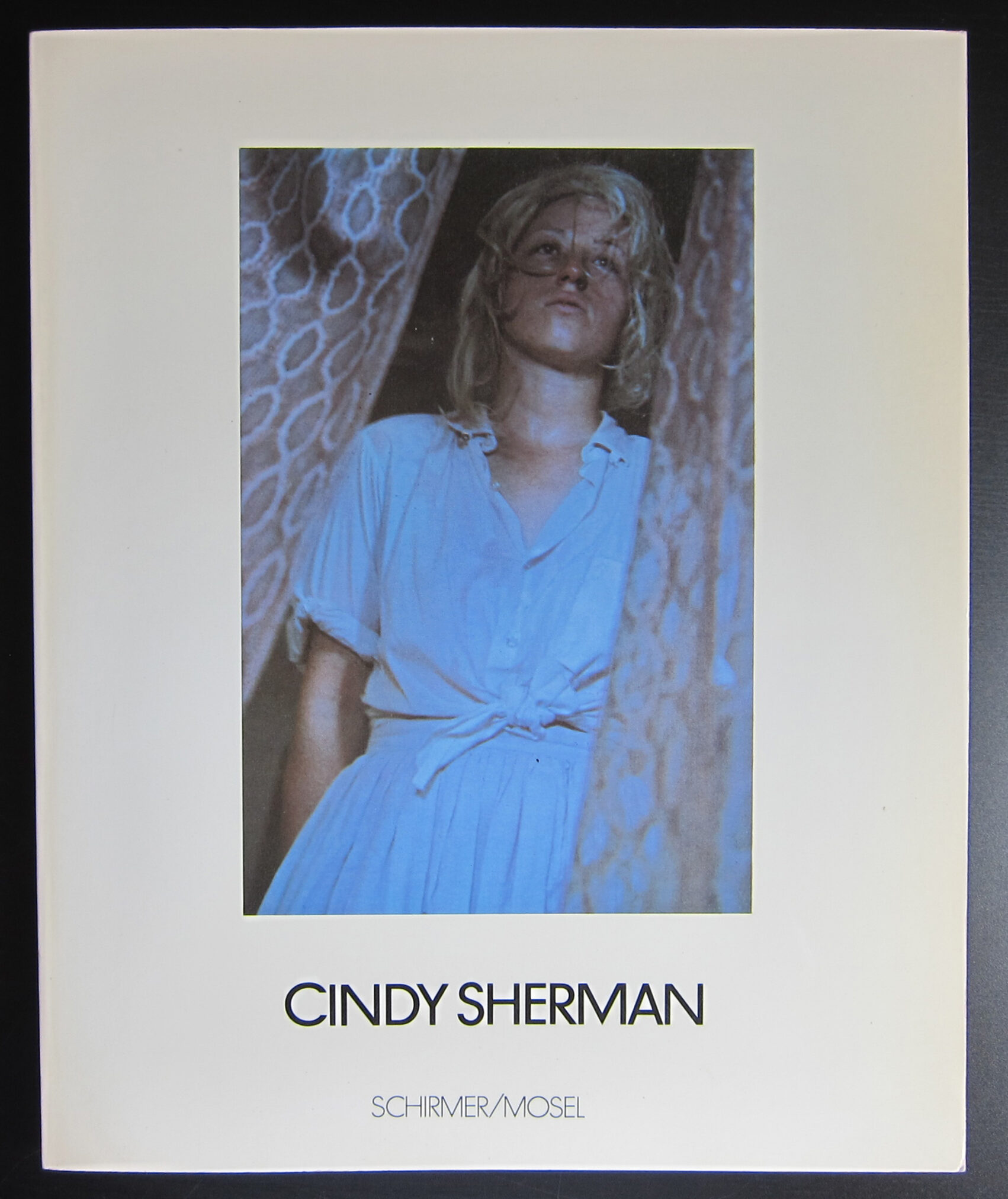 Book cover featuring a photograph of a woman in a blue dress, looking upwards with a serious expression. The image is framed by a curtain, and the title 'CINDY SHERMAN' is displayed prominently at the bottom, along with the publisher 'SCHIRMER/MOSEL'.