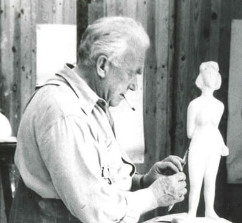 Black and white image of an artist sculpting a figure, with focus on the artist's profile and the unfinished sculpture in his hands.