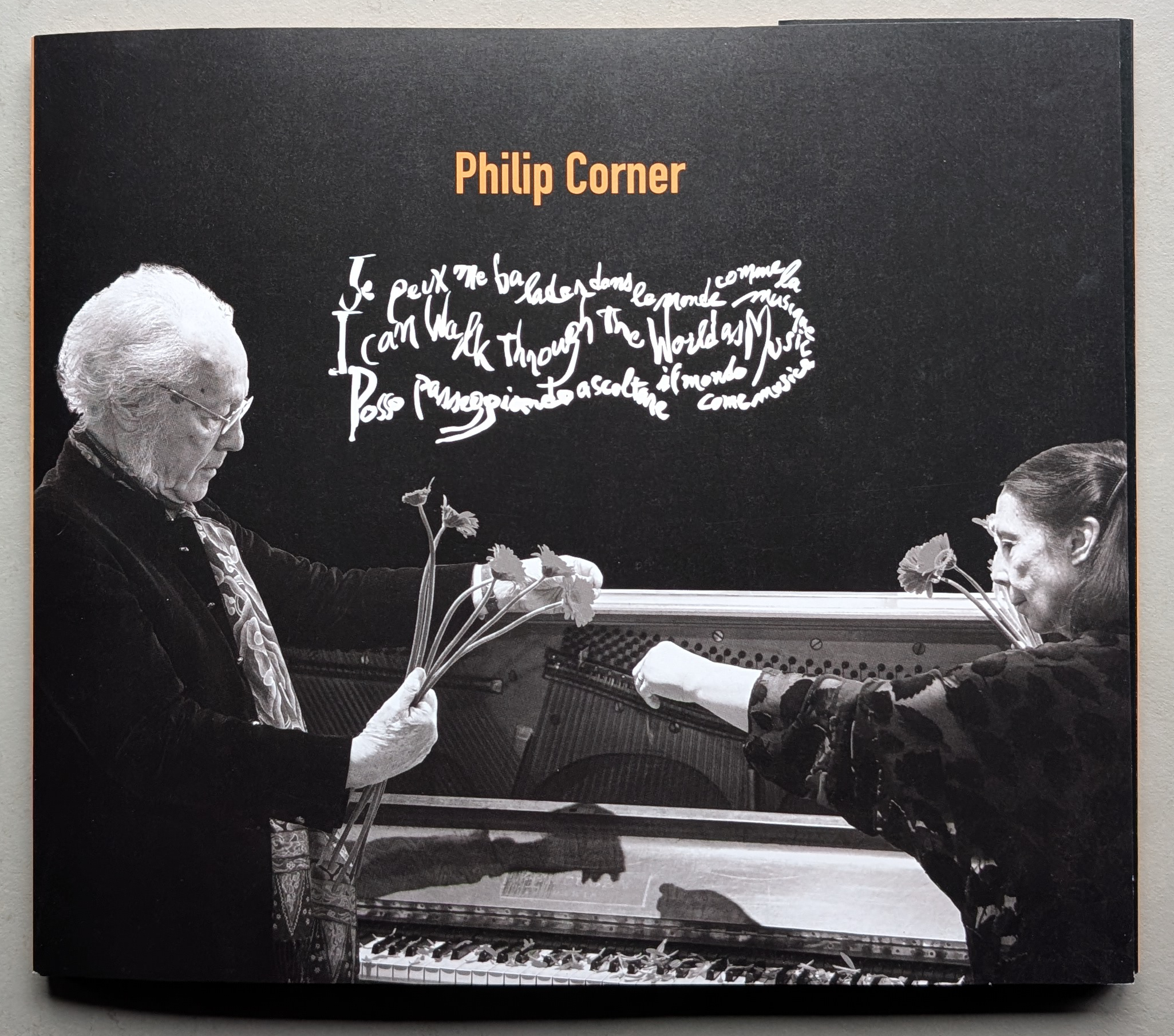 Two individuals interact with a musical instrument while holding flowers, with text in a stylized font in the background. The image is in black and white with a prominent title stating 'Philip Corner'.